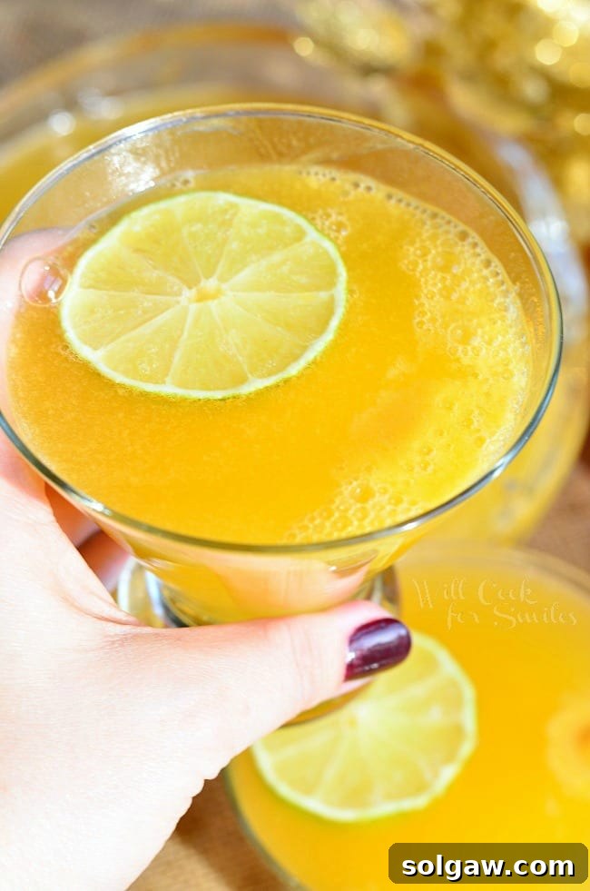 Overhead shot of a beautifully prepared Champagne Sorbet Punch in a large bowl, surrounded by fresh lime slices and elegant glasses, ready for a gathering.