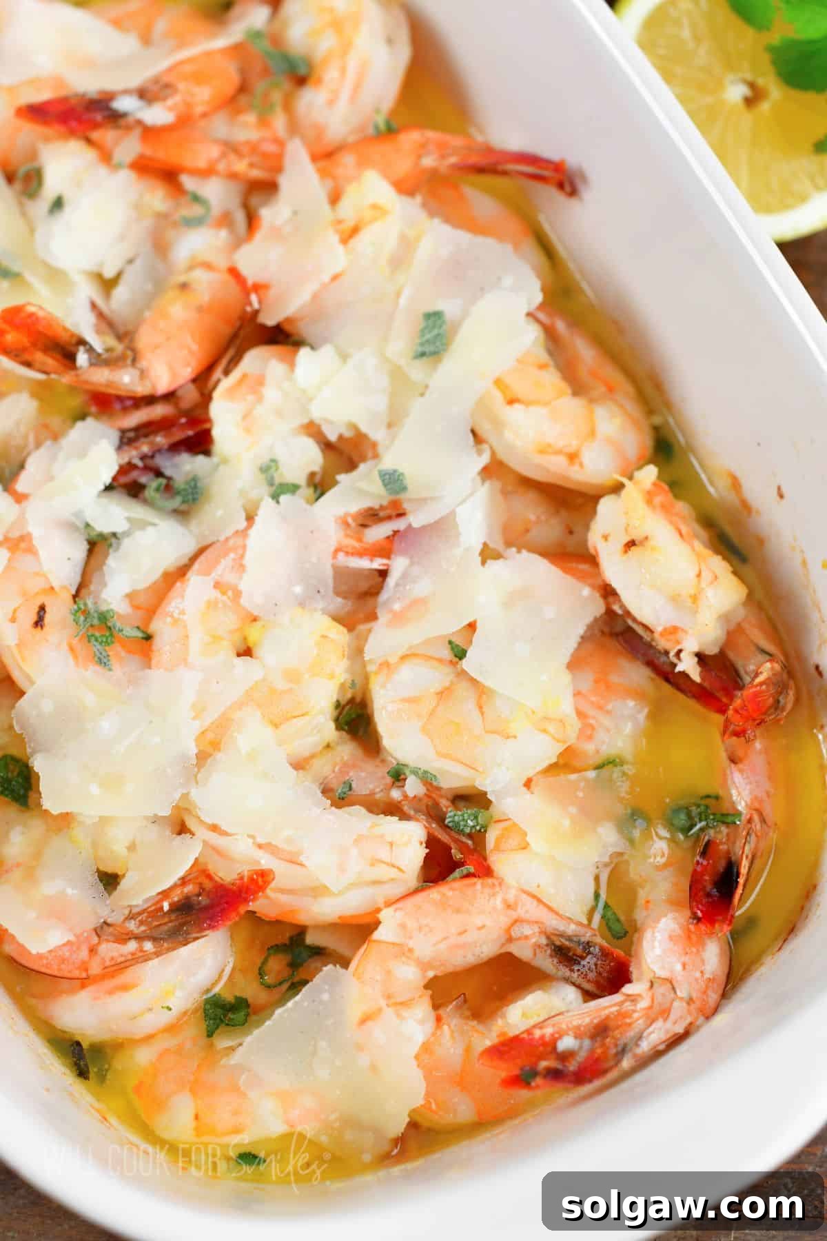 Closeup of pink shrimp baked in butter in white dish.
