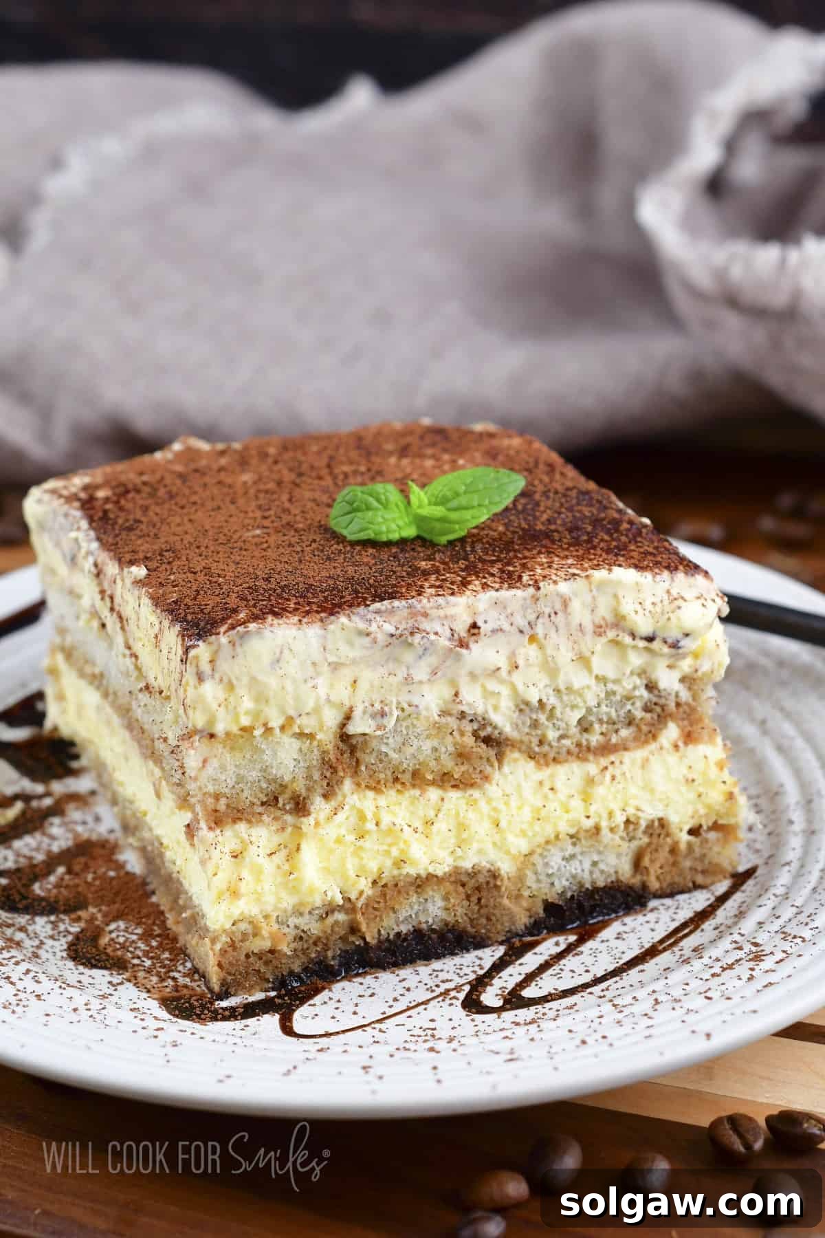 front view of a slice of tiramisu on a plate with chocolate drizzle.