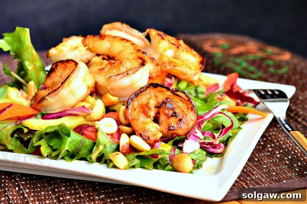 Zesty Thai Shrimp Salad with Creamy Peanut Dressing 5 close up view from the front of thai shrimp salad with peanut dressing on a red bamboo placemat and salad is on a white square plate and a fork is leaning on the right side of the plate