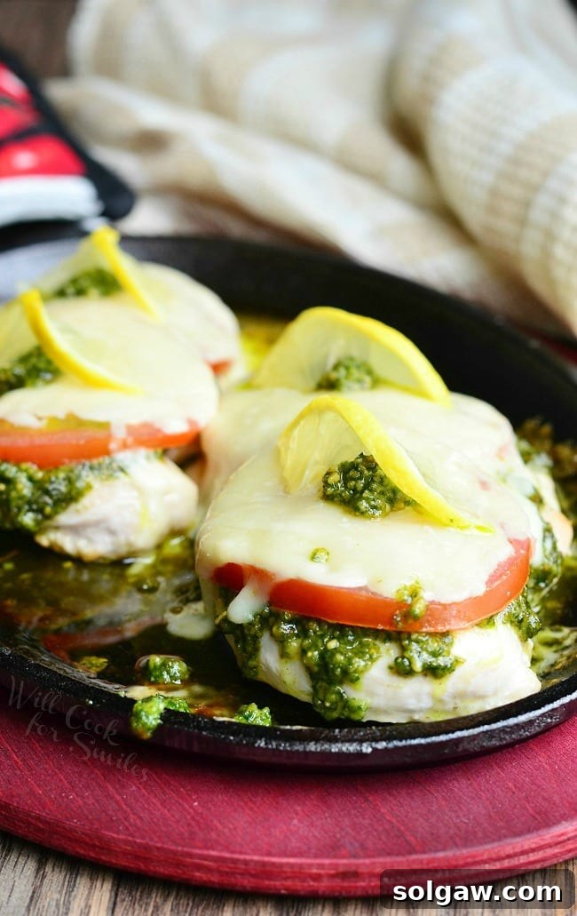 Margherita Chicken Recipe with cheese, tomato, pesto and lemon on top in a cast iron skillet 
