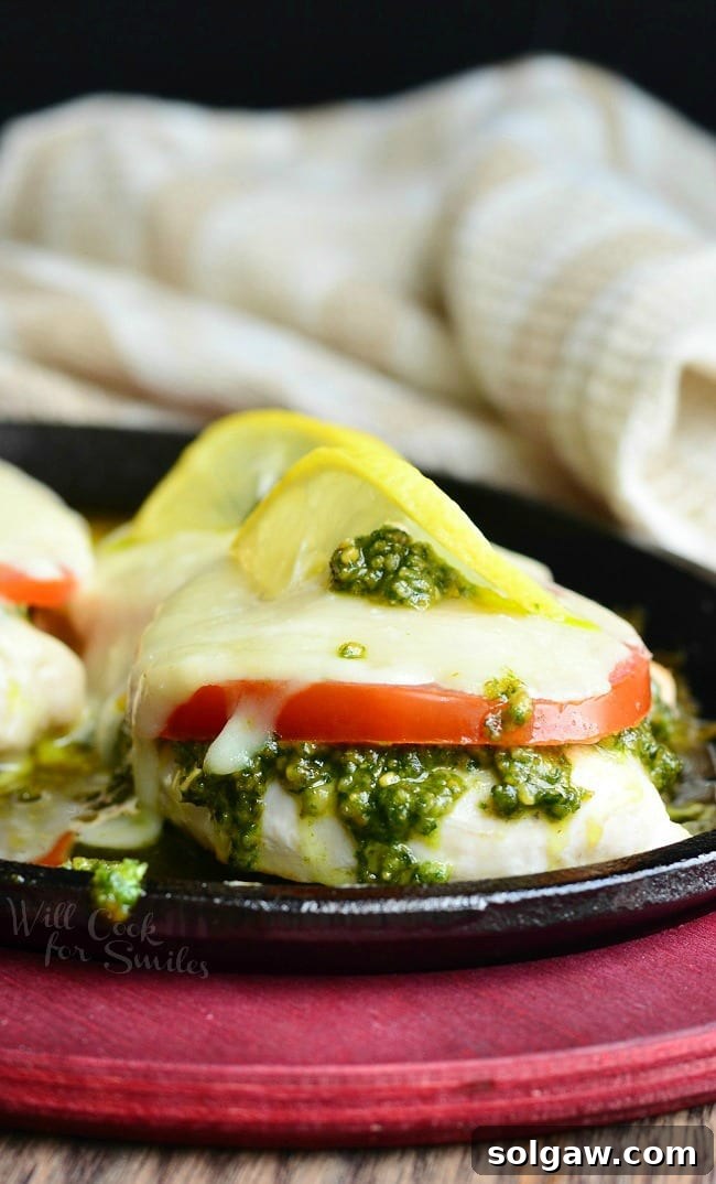 Margherita Chicken Recipe with cheese, tomato, pesto and lemon on top in a cast iron skillet 