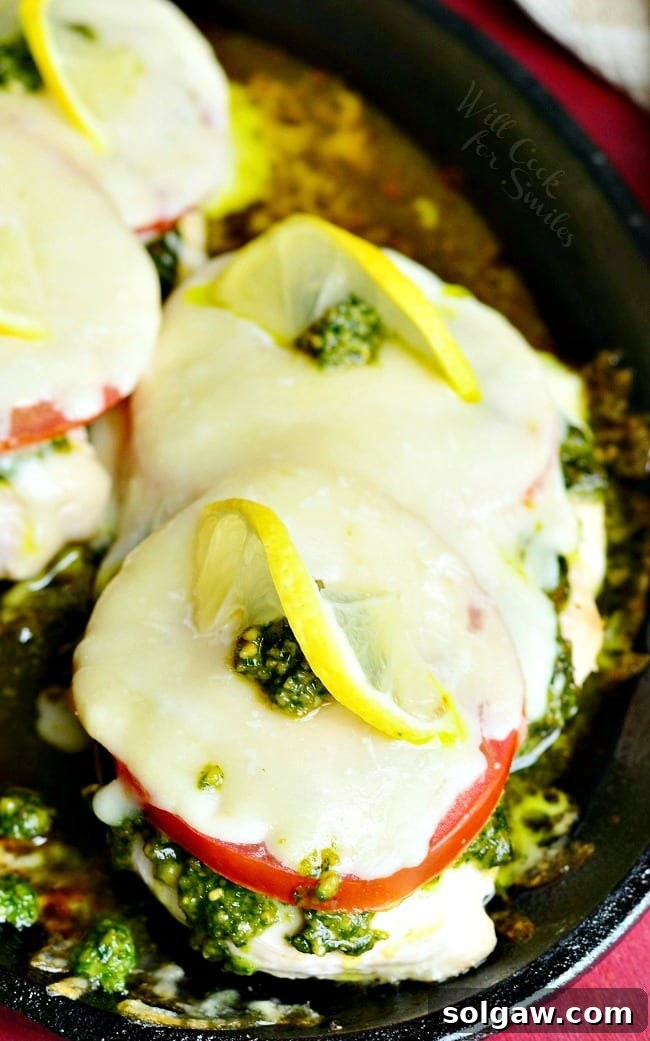 Margherita Chicken Recipe with cheese, tomato, pesto and lemon on top in a cast iron skillet 