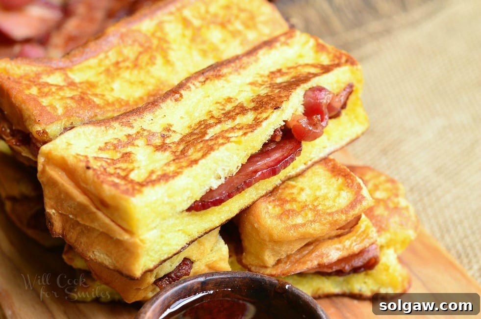 Horizontal view of a generous stack of golden French Toast sticks, each revealing a savory crispy bacon center, resting on a rustic wooden cutting board.