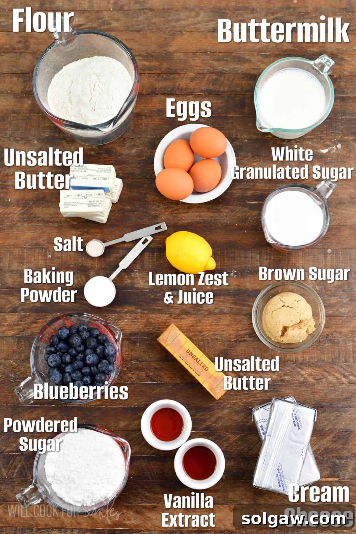 Various labeled ingredients for making a blueberry cake, including butter, eggs, flour, buttermilk, and fresh blueberries, arranged neatly on a wooden cutting board.