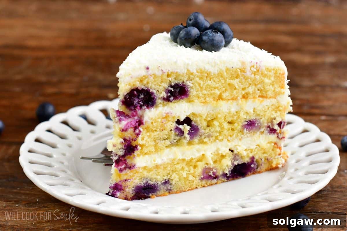 A delectable slice of blueberry cake resting on a white plate, with a scattering of fresh blueberries around it on the table, invitingly presented.