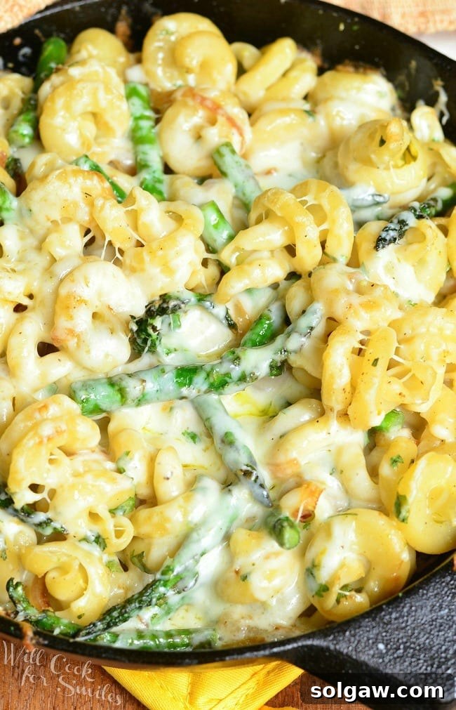 Top view of Extra Cheesy Lemon Asparagus Pasta Skillet in a black skillet. In the skillet, there are many noodles and asparagus covered in a creamy sauce, garnished with fresh herbs and a fork resting beside it.