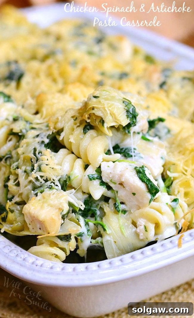Close up of Chicken Spinach and Artichoke Pasta served in a white casserole dish.