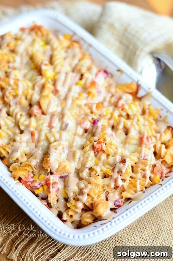BBQ Ranch Chicken Casserole served in a white casserole dish. Pasta is drizzled with a BBQ ranch sauce.
