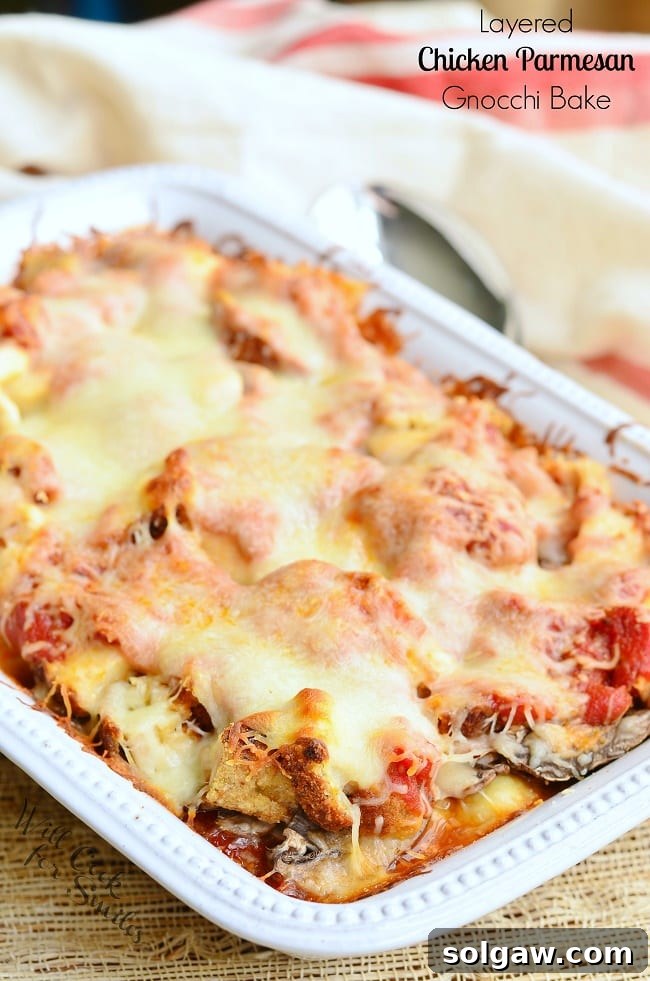 Layered Chicken Parmesan Gnocchi Bake served in a white casserole dish. The top is smothered in melted cheese.