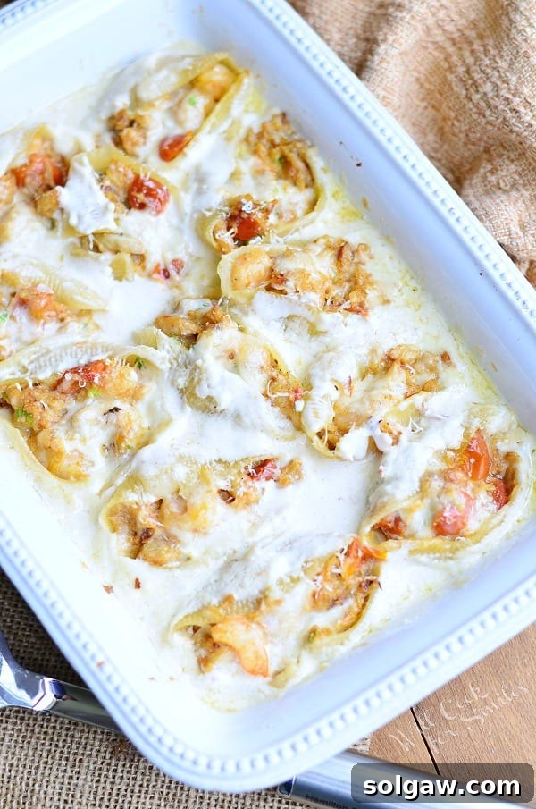 Seafood Alfredo Stuffed Shells are served in a white casserole dish. The white Alfredo sauce covers the pasta well. 