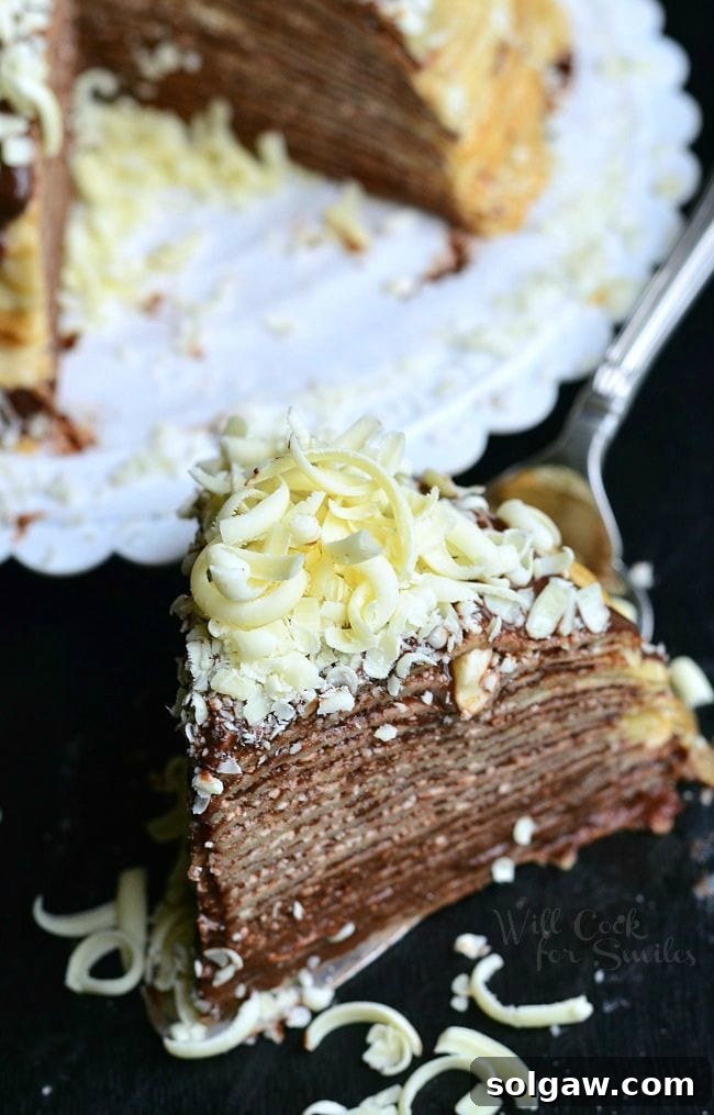 Top view of a slice of the Double Chocolate Chocolate Pudding Crepe Cake sitting on a serving spatula. The stacked crepes make for thin layers. Chocolate is a key element of this cake. It's between all layers and then on top as well. There are also white chocolate shavings on top of this slice of cake.