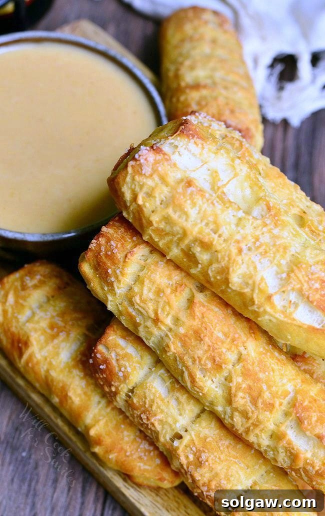 Top view of a mound of Homemade Soft Pretzels placed on a wooden board. Pretzels are a nicely golden brown. Next to the pretzels is a bowl of beer cheese dip.