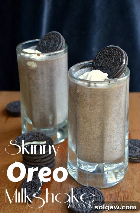 two Oreo Milkshake in a glass mug with whipped cream and an oreo as garnish on a wood table with oreos all around it