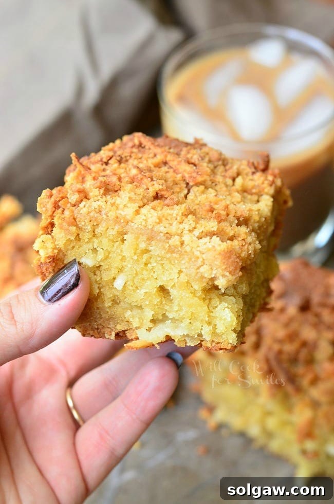 Espresso Caramel Swirl Cheesecake Bars 7 The left hand is holding a piece of Coconut Coffee Cake for a close up. In the background is more of the cake and an iced coffee.