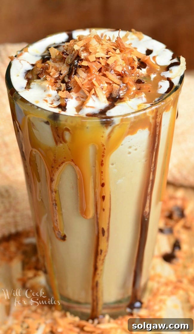 Espresso Caramel Swirl Cheesecake Bars 8 Samoas Frozen Coffee is in a tall glass that is filled to the brim. Caramel and chocolate run down the sides of the glass. It is topped off with more drizzles of caramel, chocolate and toasted coconut flakes.