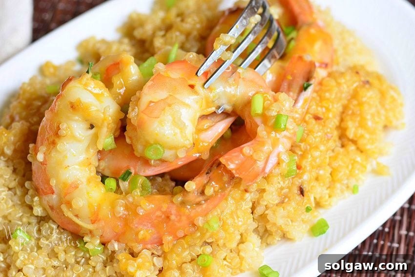 Citrus-Kissed Shrimp with Fiery Quinoa 3 Close-up of Orange Shrimp with Quinoa in a white bowl with a fork in one of the shrimp, highlighting the texture and color