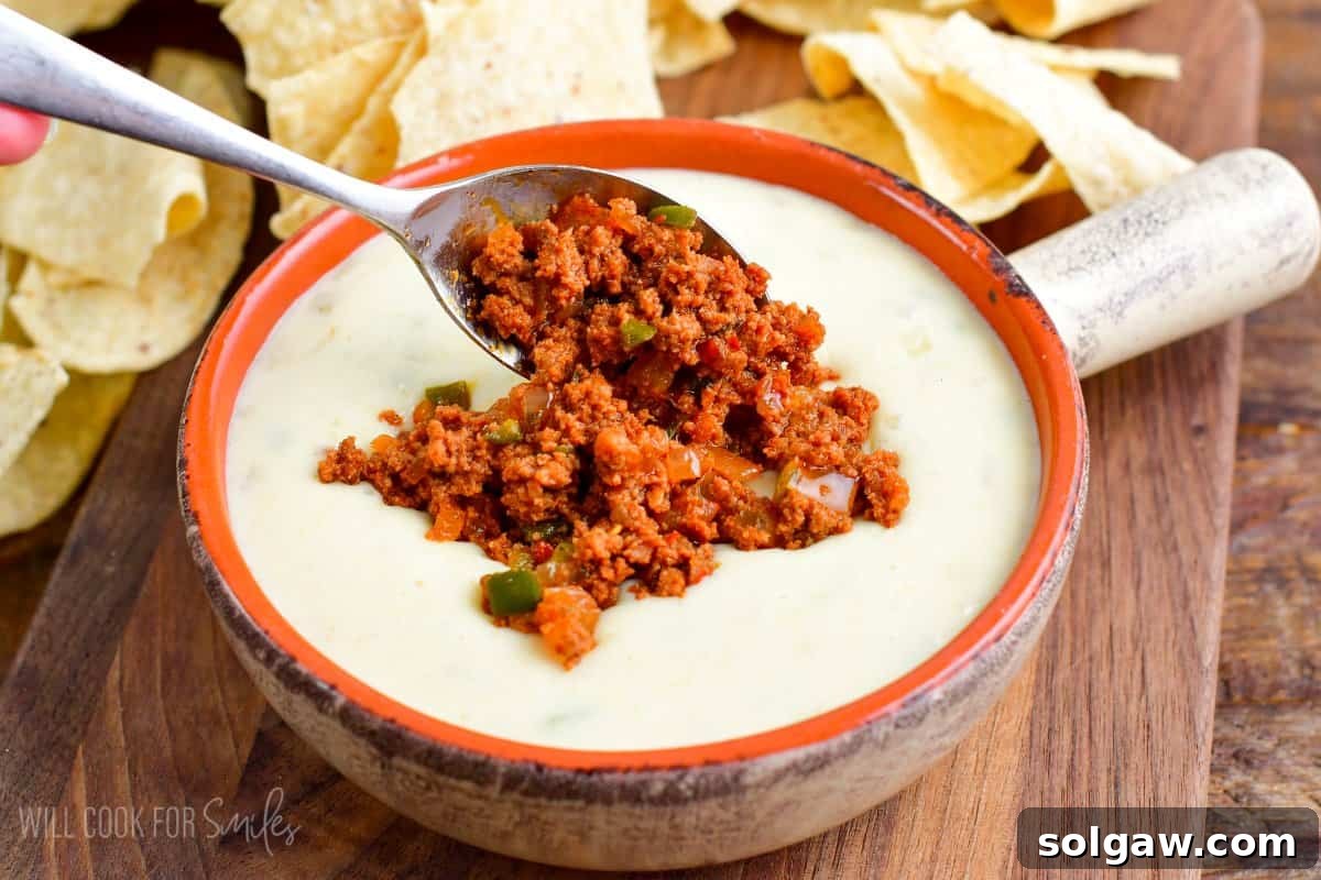 Cooked chorizo, peppers, and onions being generously added on top of a serving bowl filled with creamy white queso dip.