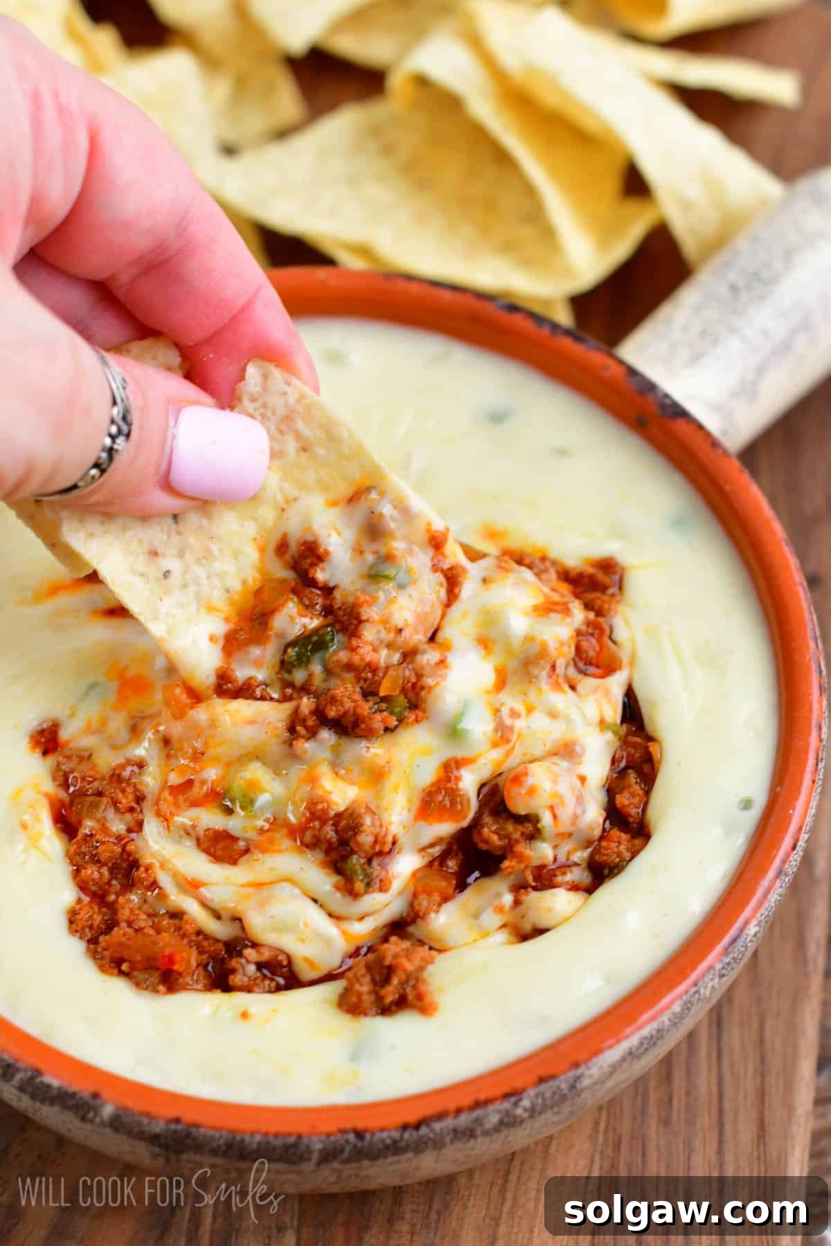 A tortilla chip generously loaded with creamy Queso Blanco swirled with savory chorizo sausage, ready to be enjoyed.