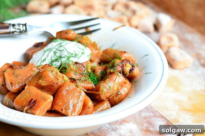 Handcrafted Tomato Herb Gnocchi Pillows 4 Vertical photo of Tomato Herb Gnocchi cooked and served in a white bowl with a dollop of sour cream and fresh dill on top, a fork resting behind it on a wooden table