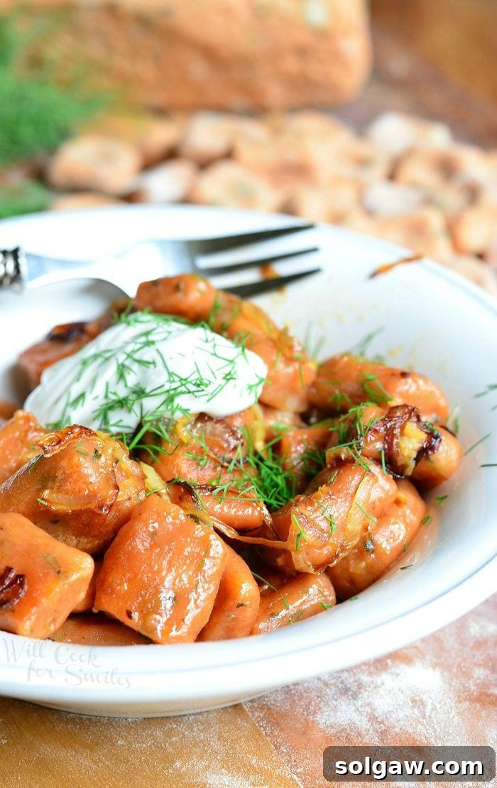 Handcrafted Tomato Herb Gnocchi Pillows 6 Close-up photo of Tomato Herb Gnocchi cooked in a white bowl with sour cream and dill on top, a fork in the background on a wood table