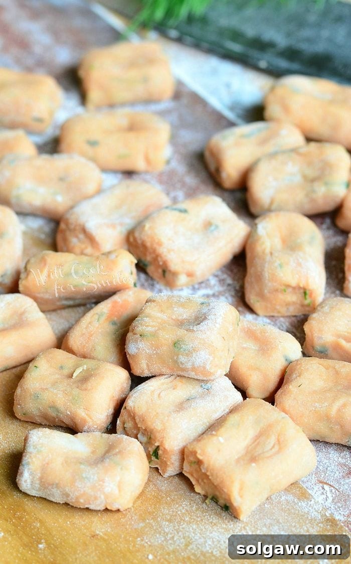 Handcrafted Tomato Herb Gnocchi Pillows 7 Uncooked Tomato Herb Gnocchi pieces arranged neatly on a cutting board, dusted lightly with flour