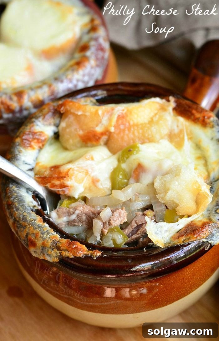 2 clay crocks filled with philly cheese steak soup on a wooden cutting board with a spoon resting inside first crock revealing contents of soup