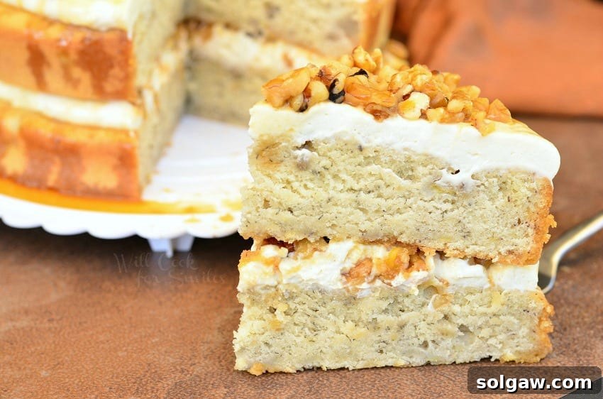 A close-up view of a slice of Caramel Banana Nut Cake on a white plate, highlighting the moist cake texture and creamy frosting