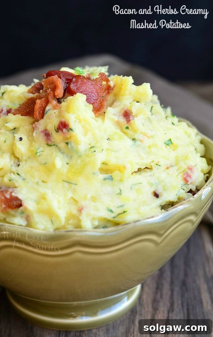 A close-up view of creamy mashed potatoes generously topped with crispy bacon bits and fresh green herbs, served in a rustic bowl.