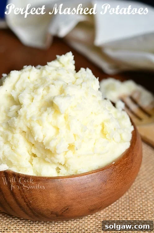 A simple wooden bowl filled with perfectly smooth and creamy mashed potatoes.
