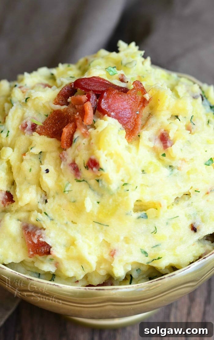 A side shot of creamy mashed potatoes with bacon and herbs in a bowl, showcasing the inviting texture and garnish.