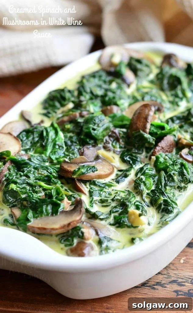 white baking pan filled with creamed spinach and mushroom in white wine sauce on a wooden table with a white cloth behind