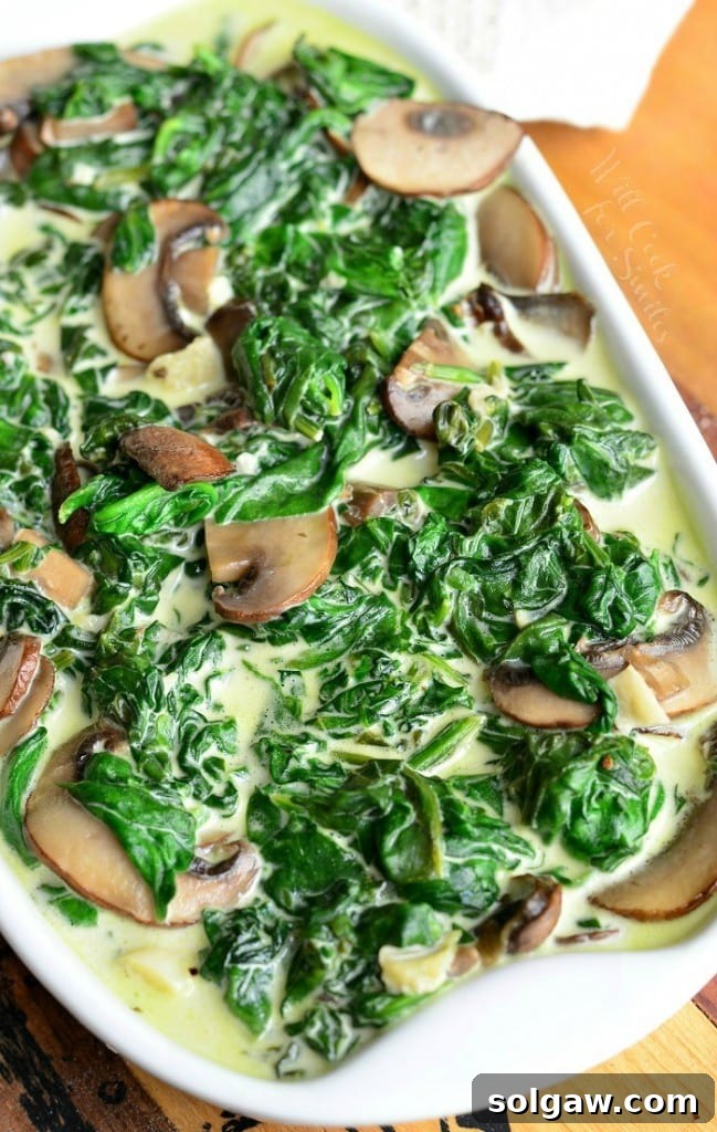 white baking pan filled with creamed spinach and mushroom in white wine sauce on a wooden table with a white cloth behind as viewed from above