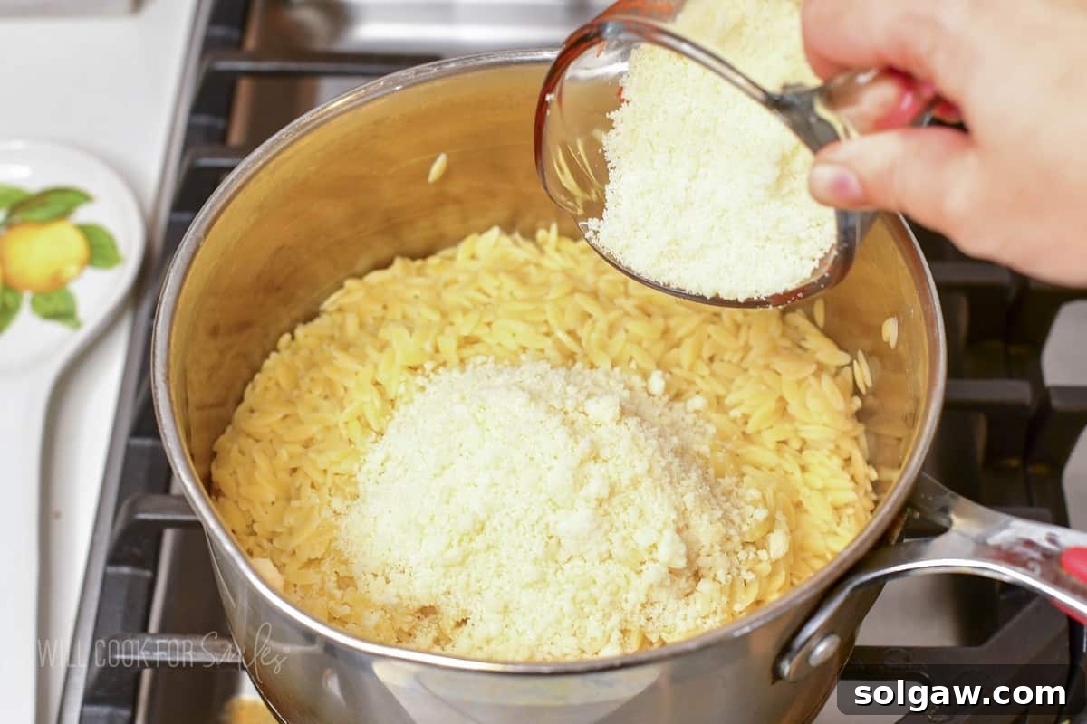 adding grated parmesan to hot orzo in a pot, showing the cheese melting into the pasta.