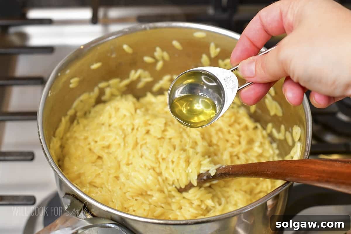 adding some truffle oil to the orzo with cheese, showing the final flavoring step.