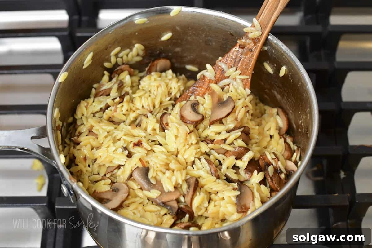 mixing mushrooms into parmesan orzo, ensuring all ingredients are well combined.