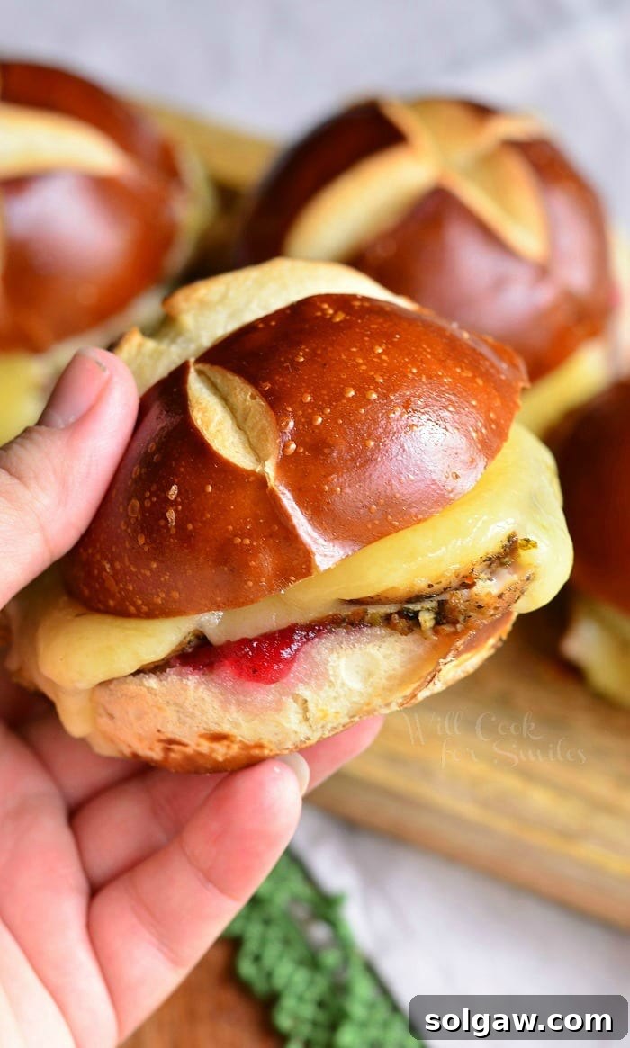 Holding a Cranberry Asiago Turkey Sliders that's on a pretzel bun, ready to be eaten