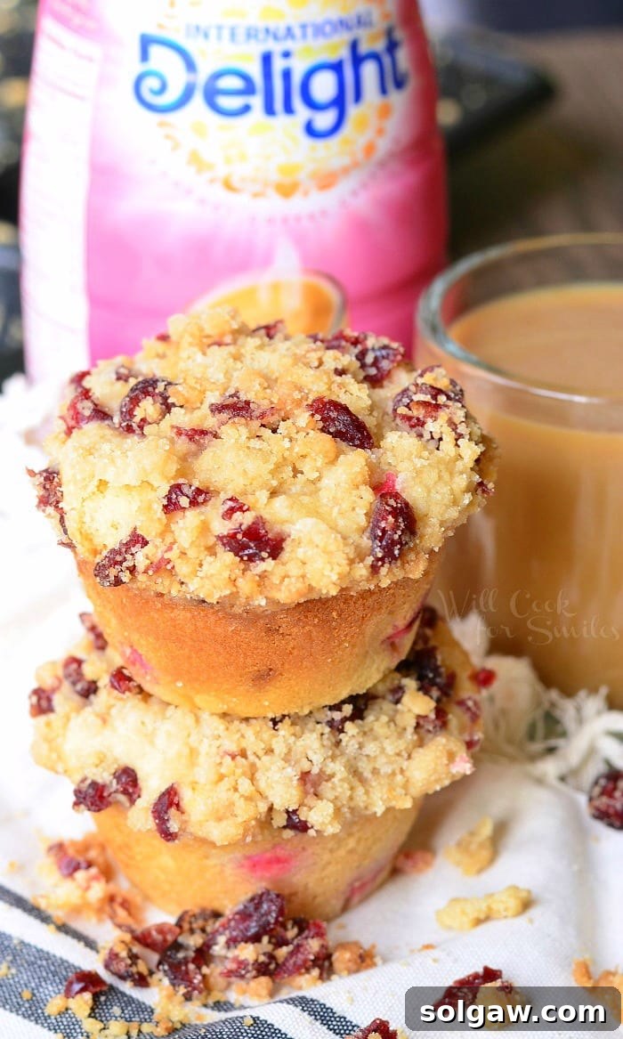 Cranberry White Chocolate Chip Streusel Muffins stacked beside a glass of coffee, showcasing their beautiful streusel topping.