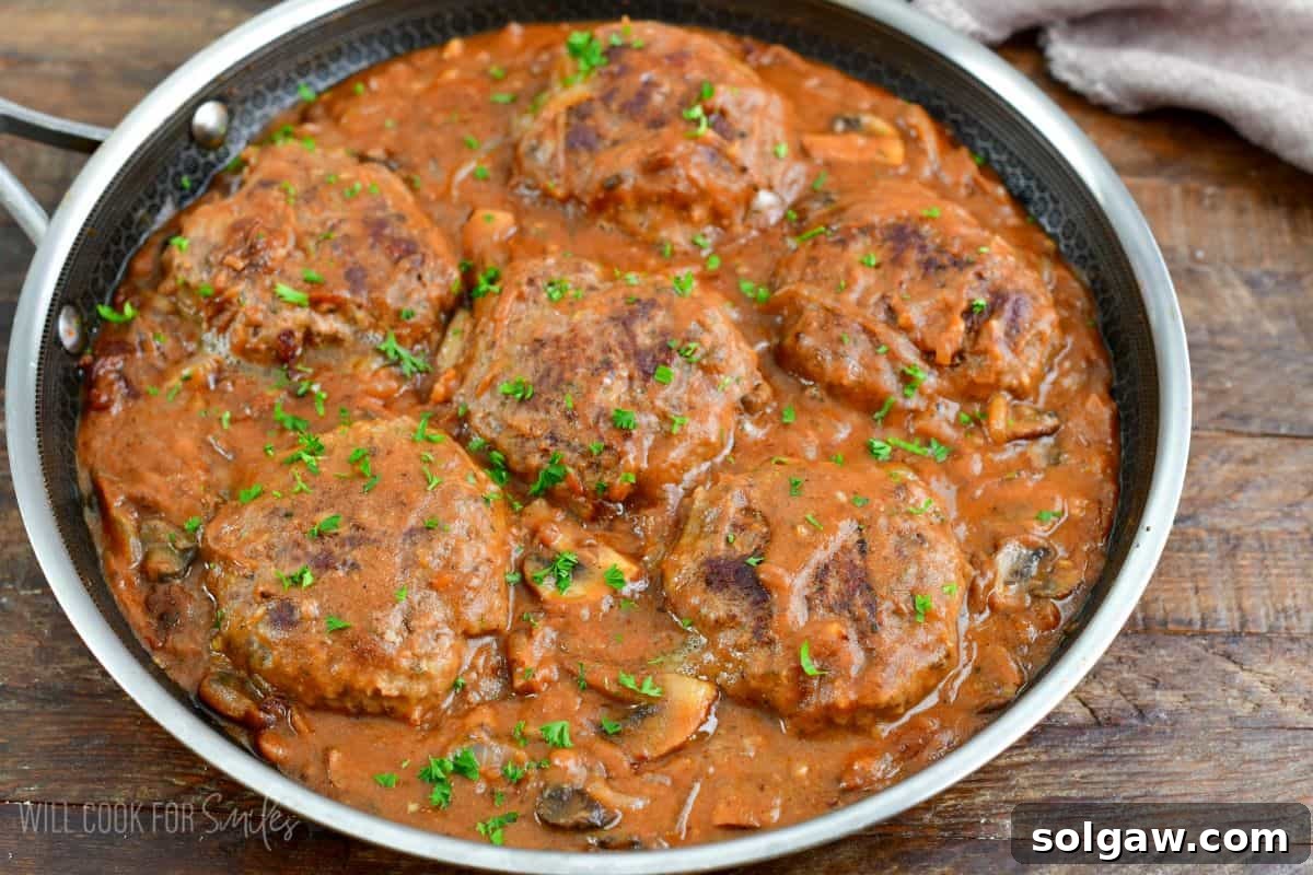 Salisbury steaks in a pan with gravy on a wood surface.