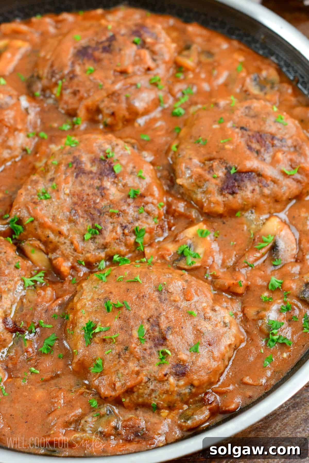 Salisbury Steak in a pan top with parsley on top on a wood surface.