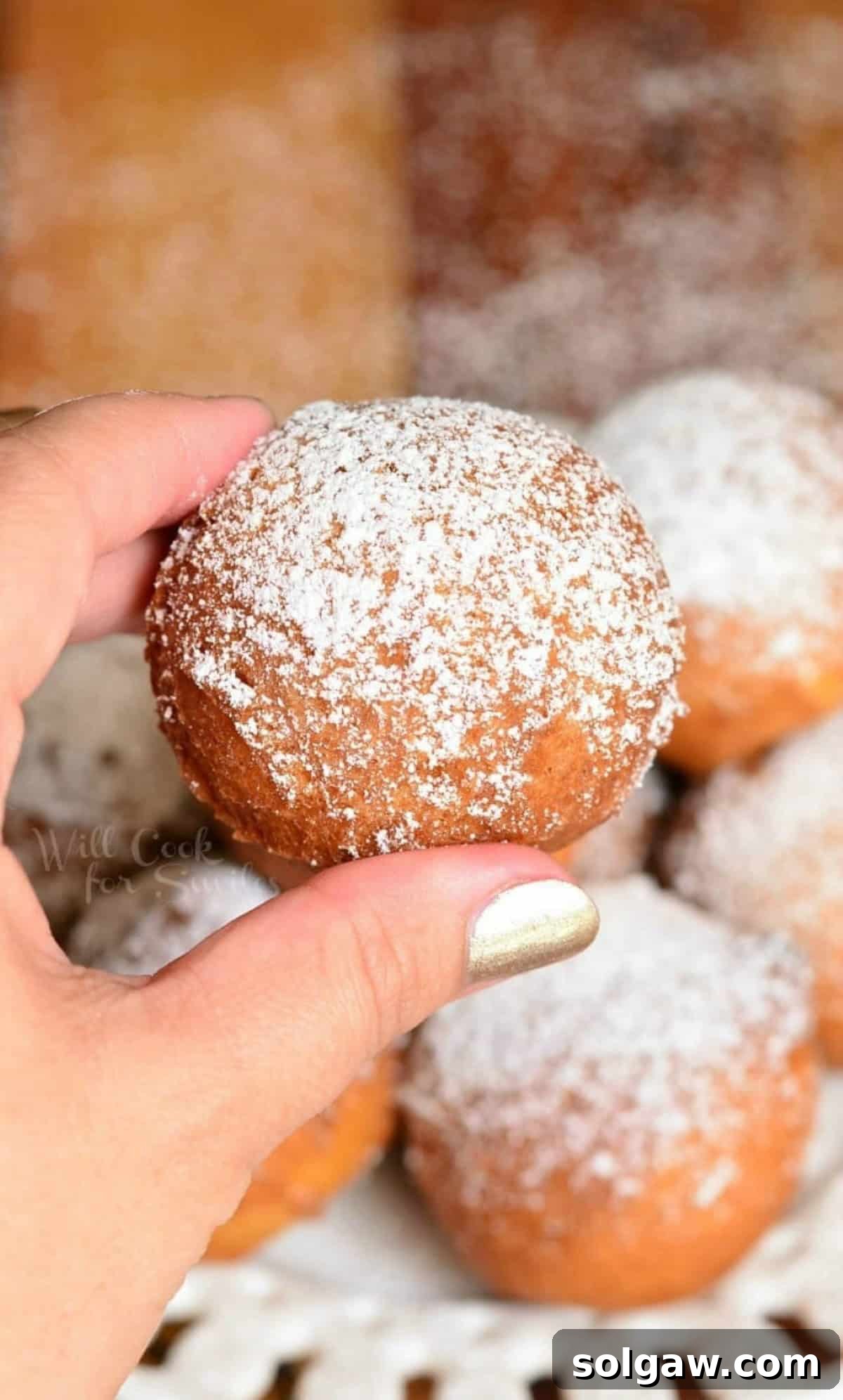 holding one doughnut hole over the plate of more.