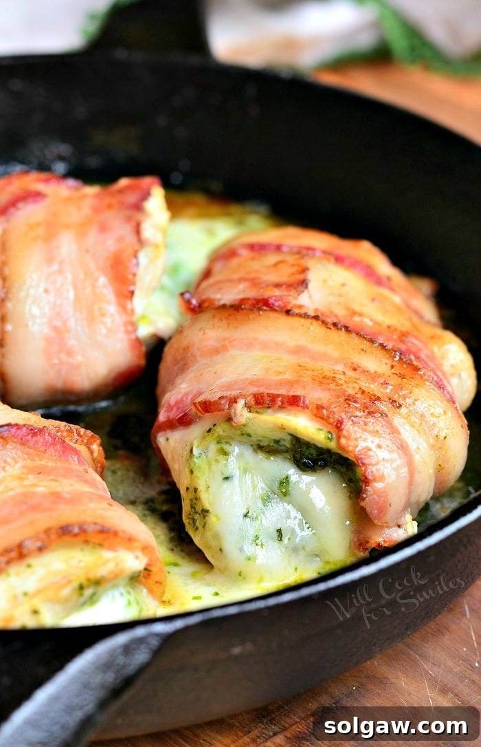Bacon Wrapped Pesto Mozzarella Stuffed Chicken Breast in a cast iron pan, fresh from the oven, with melted cheese and crispy bacon.