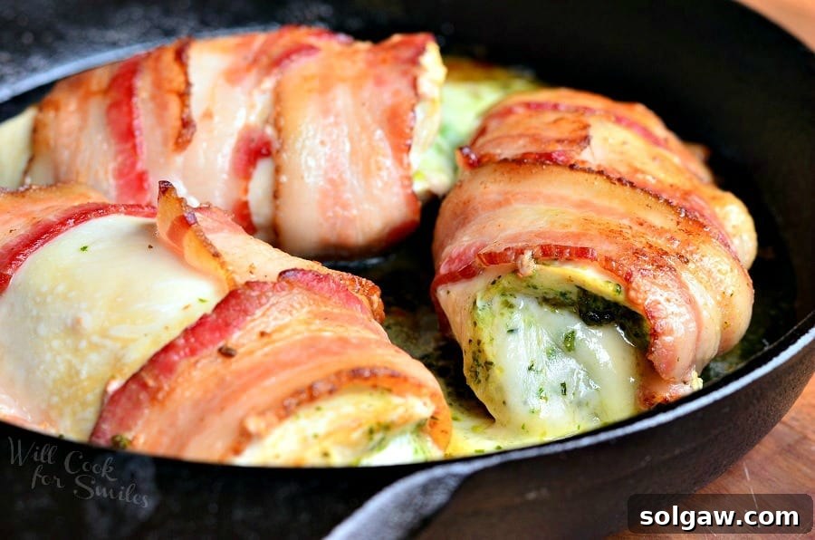 Bacon wrapped chicken breast with cheese and pesto, served with a side of green vegetables on a white plate.
