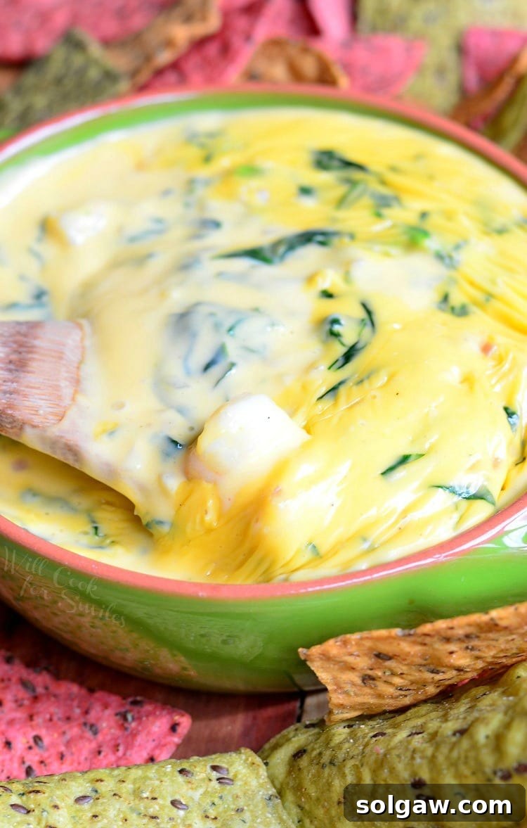 Shrimp and Spinach Queso Dip in a vibrant green bowl, surrounded by crispy tortilla chips and a rustic wooden spoon.