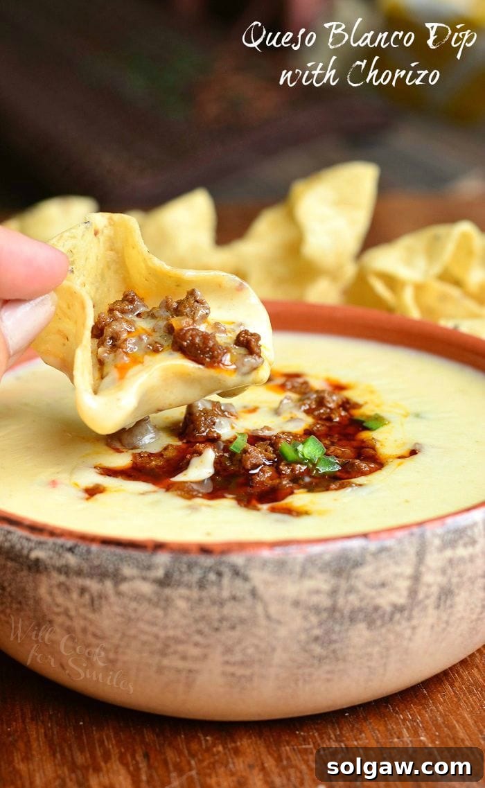 A tortilla chip being dipped into a rich Queso Blanco Dip with Chorizo.