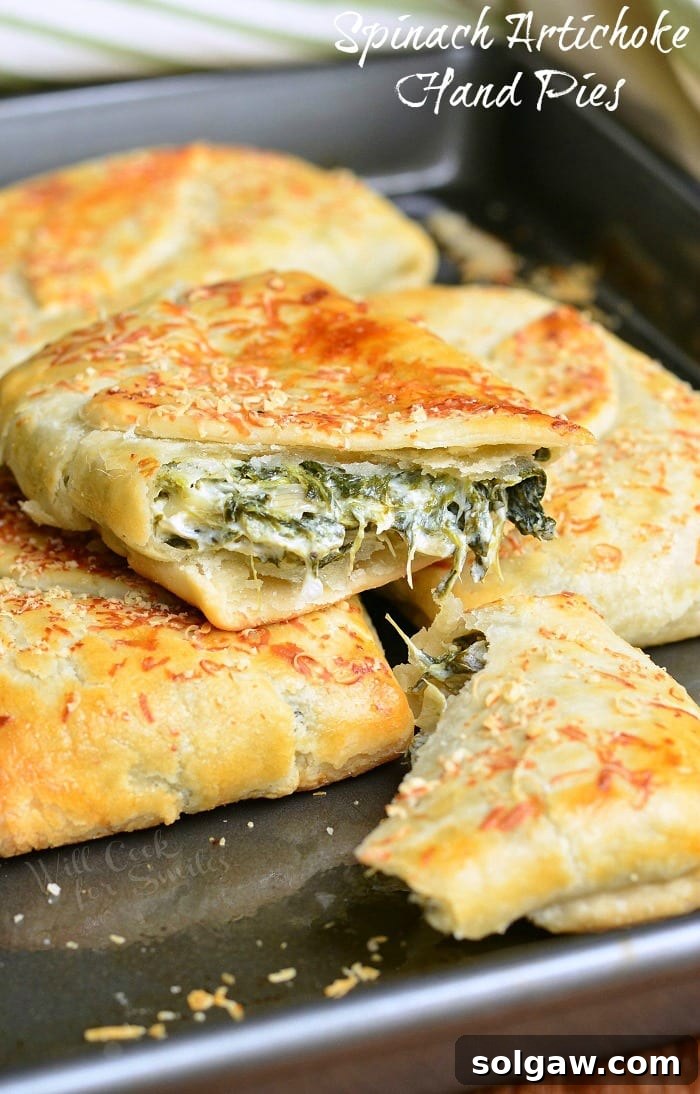 Golden brown Spinach Artichoke Hand Pies neatly arranged on a baking sheet.