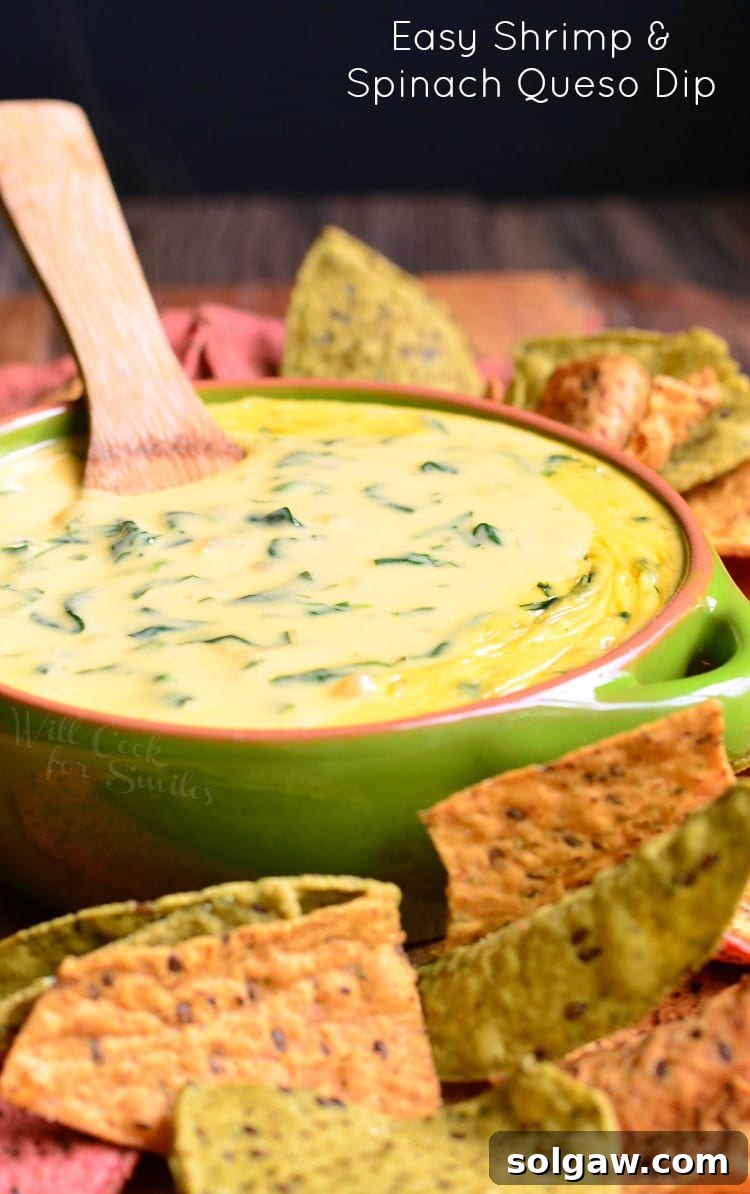 Shrimp and Spinach Queso Dip served in a green bowl, with a wooden spoon and an abundance of tortilla chips ready for dipping.