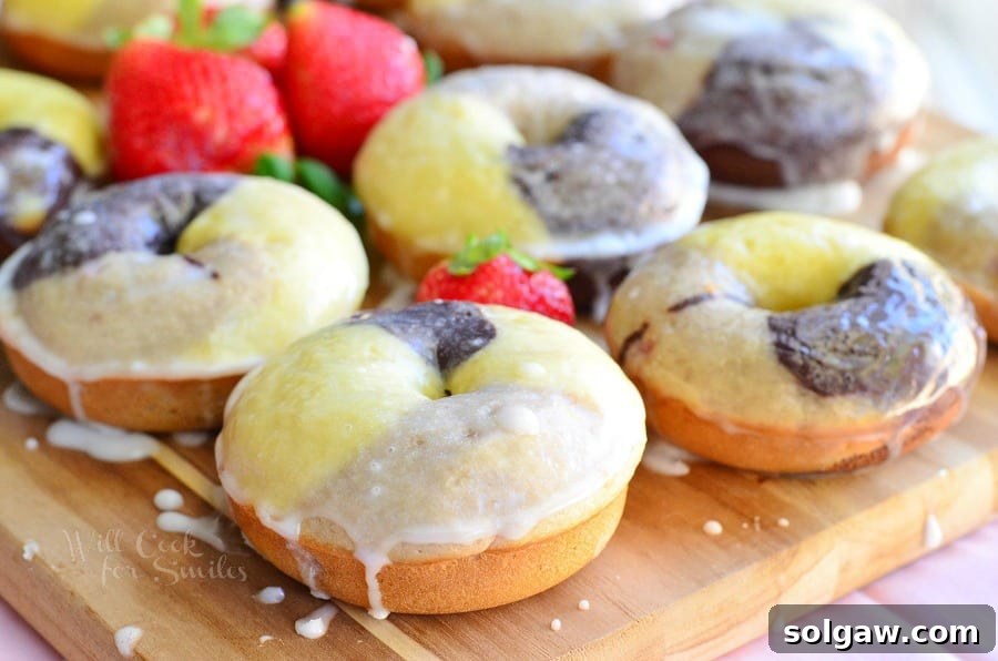 Freshly baked Neapolitan Glazed Doughnuts cooling on a wire rack, with vibrant red strawberries scattered around, visually emphasizing the strawberry flavor.