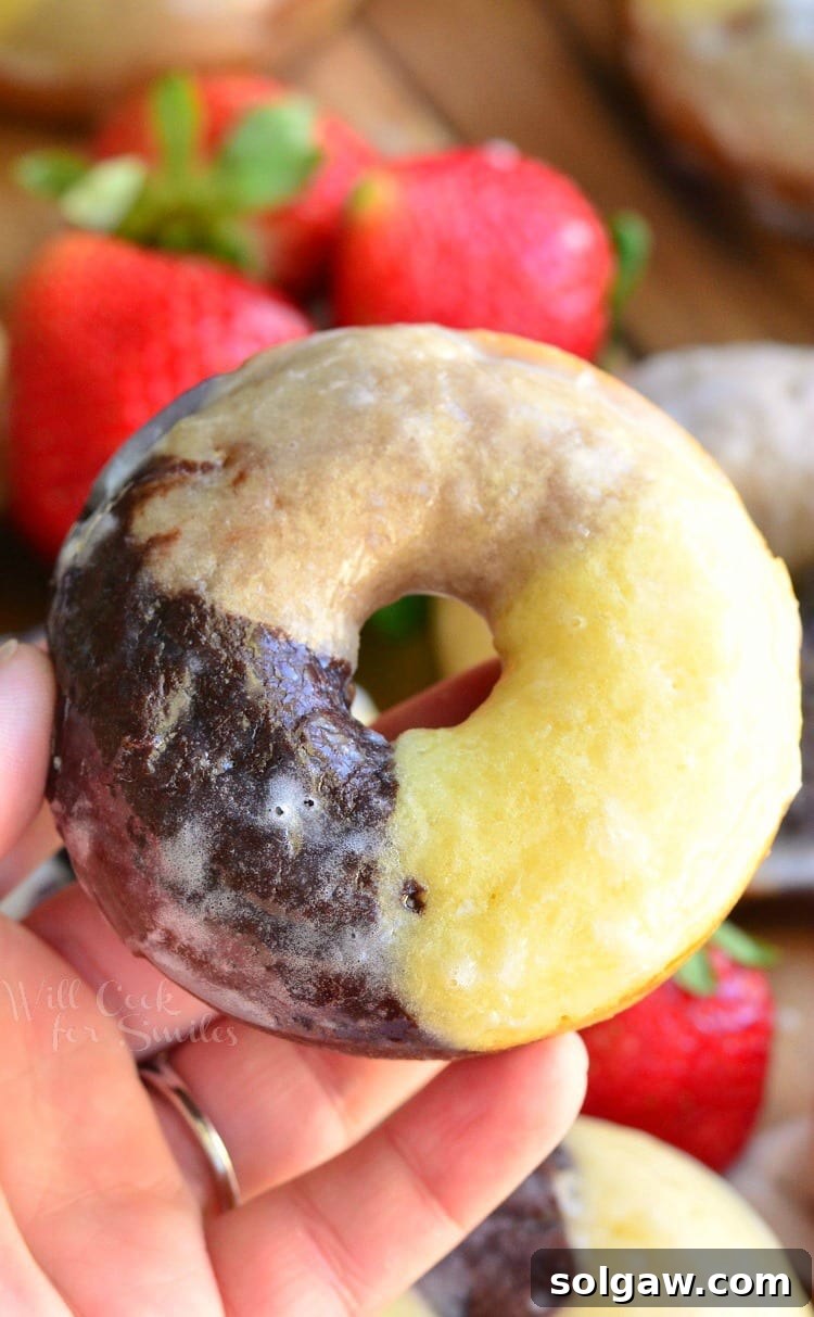 Baked napoleon glazed doughnuts glazed on a wooden cuttingboard with strawberries in the background and a hand hold one doughnut above the rest