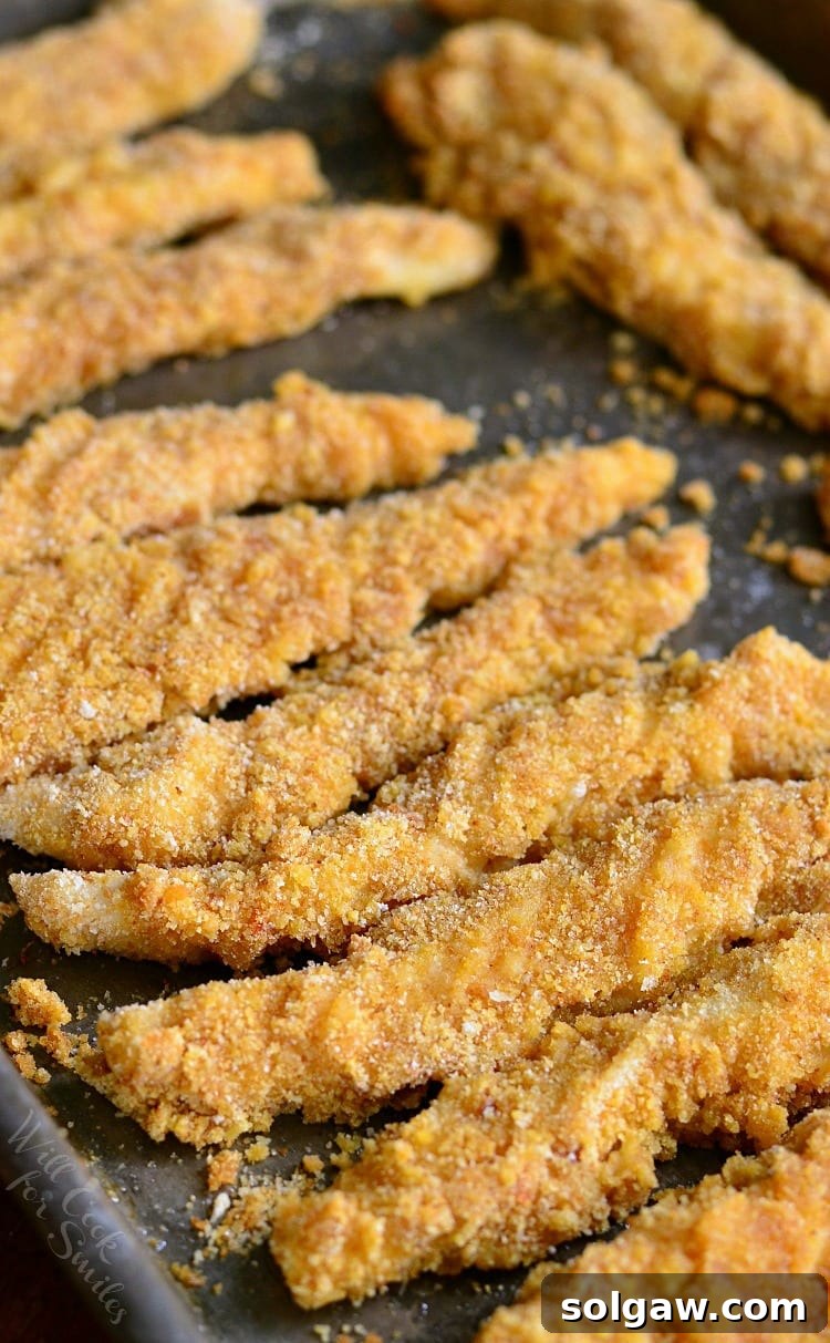 A close-up shot of crispy, golden chicken fries baking to perfection on a large baking sheet, fresh from the oven.